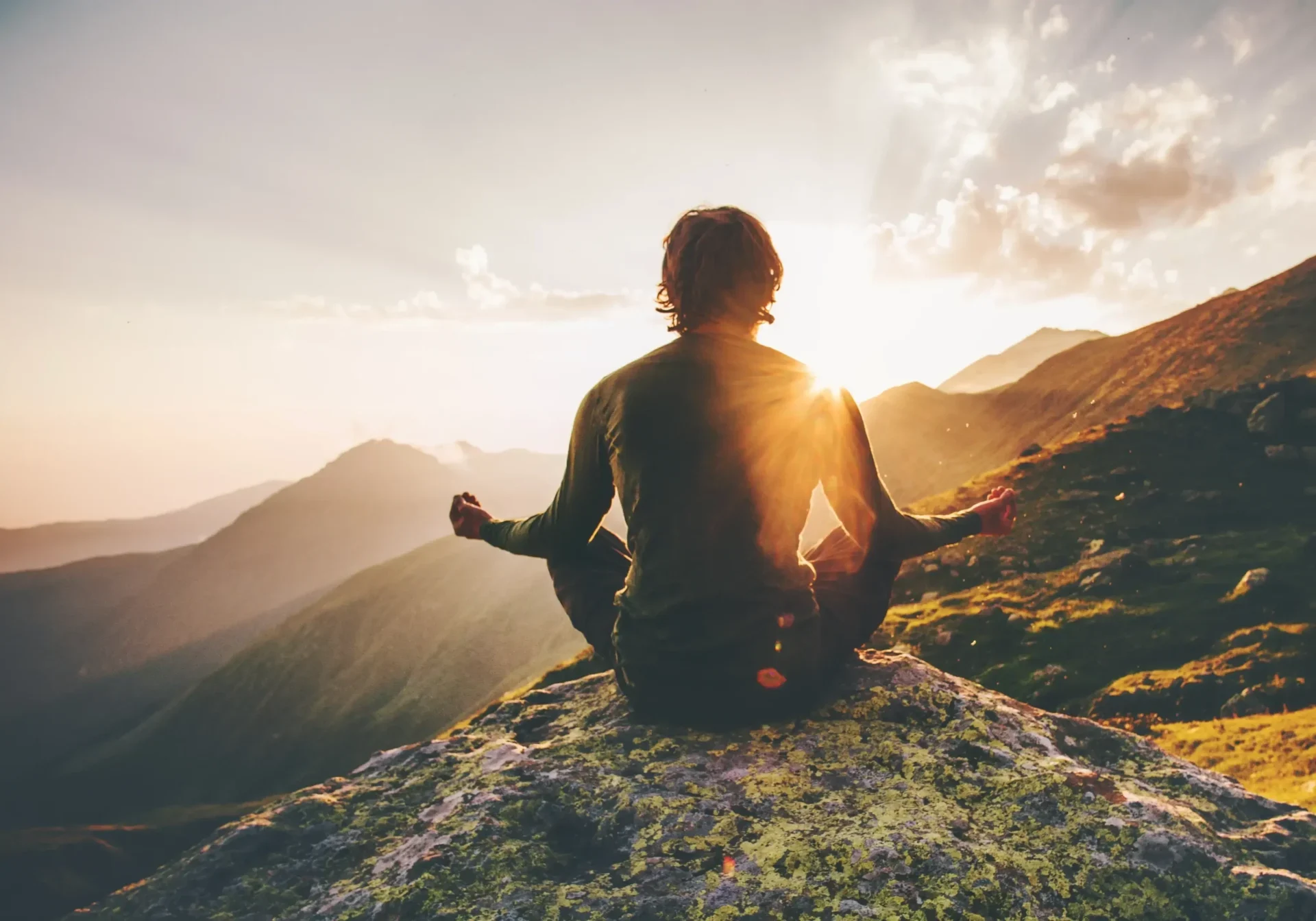 A person sitting on top of a mountain with the sun setting.